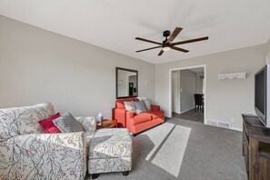 Ein Wohnzimmer mit einer Couch, einem Hocker und einem Fernseher.