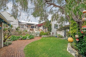 A residential garden with a paved pathway, a grassy lawn, and a stone wall. - Saltwood: Yallingup Garden Sanctuary by the Sea (Yallingup)