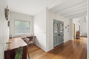A room with a wooden desk, a chair, a window with blinds, and a blue door with decorative elements. - Saltwood: Yallingup Garden Sanctuary by the Sea (Yallingup)