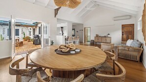 A spacious dining area with a round wooden table, wicker chairs, and a hanging light fixture. - Saltwood: Yallingup Garden Sanctuary by the Sea (Yallingup)