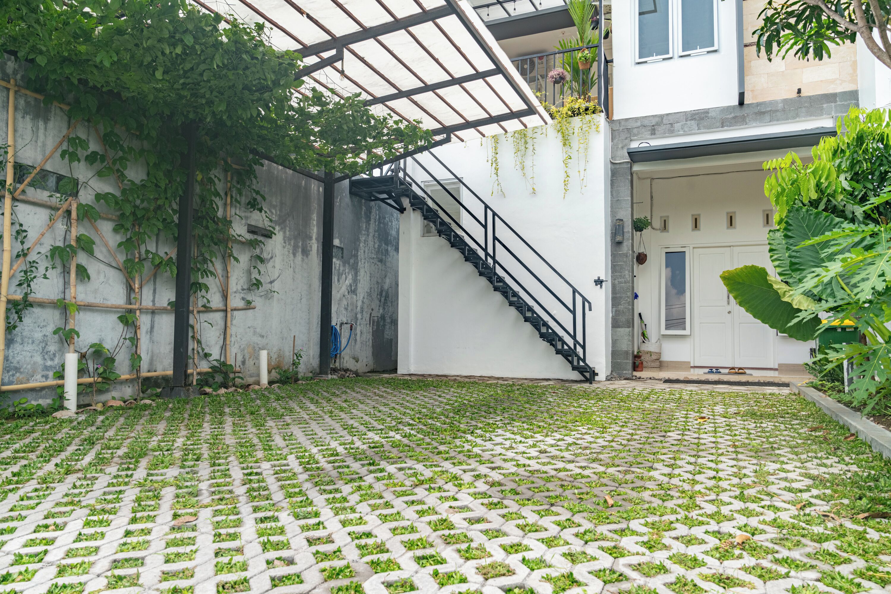 Un patio con piso de baldosas, una escalera y un edificio blanco con puerta y ventanas.