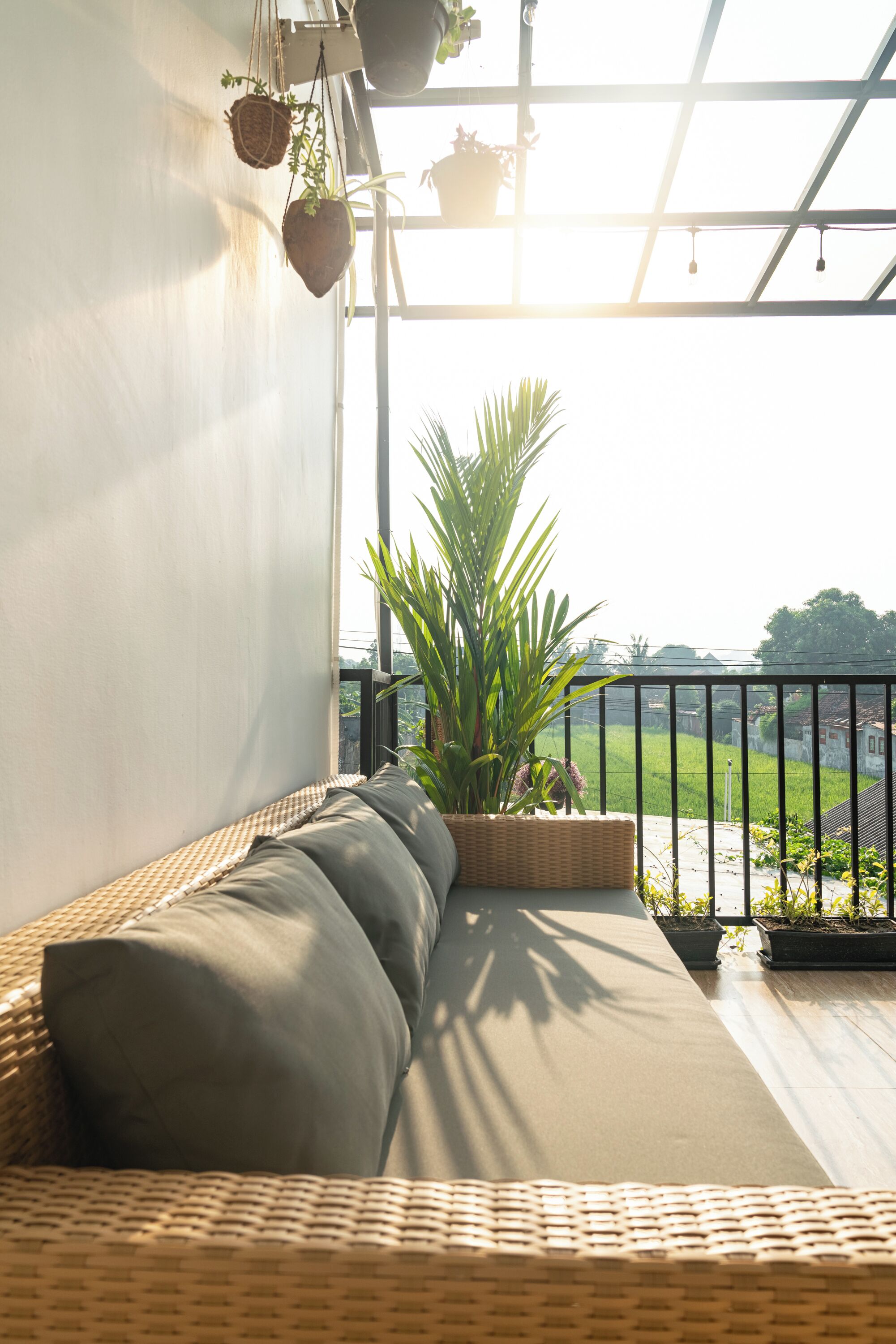 Un balcón con un sofá de mimbre, plantas en macetas y vistas a un paisaje verde.