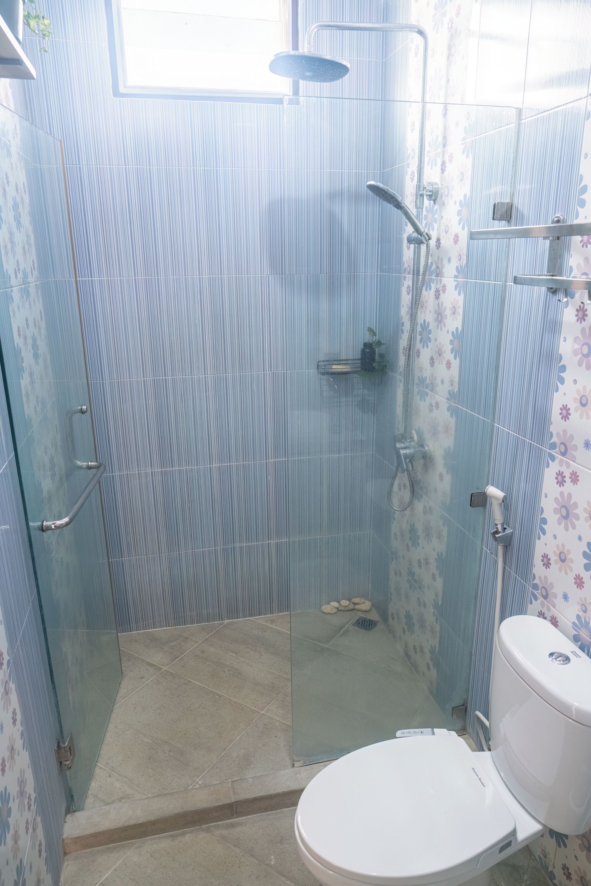 Un baño con ducha envuelta en vidrio, inodoro y paredes con azulejos.