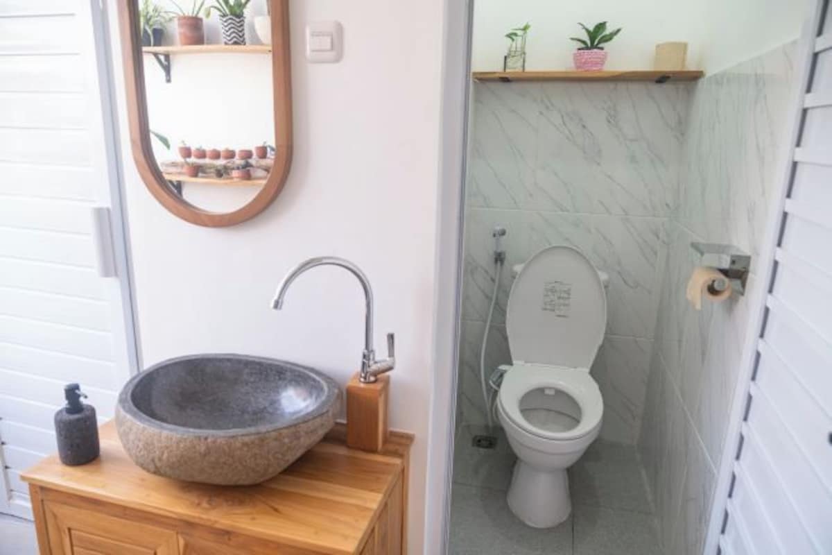 A bathroom with a stone sink, wooden vanity, a mirror, a toilet, and a shower area.