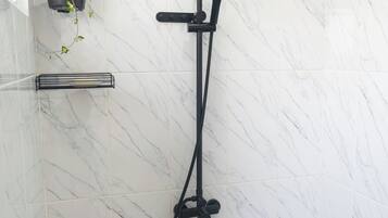 A modern bathroom with a black showerhead, a marble wall, and a shelf with plants.