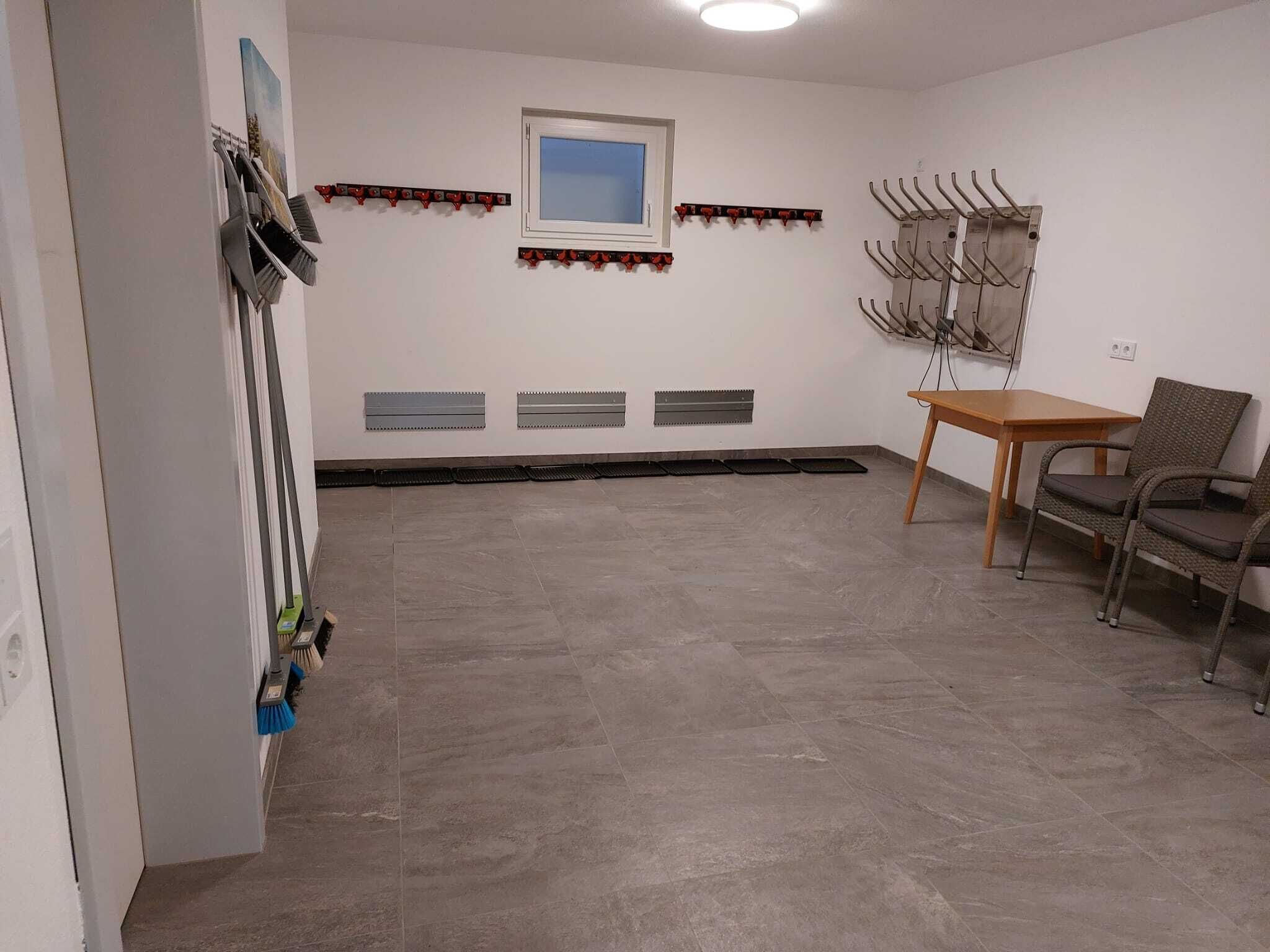 A room with a tiled floor, a window, a coat rack, a chair, and a table.