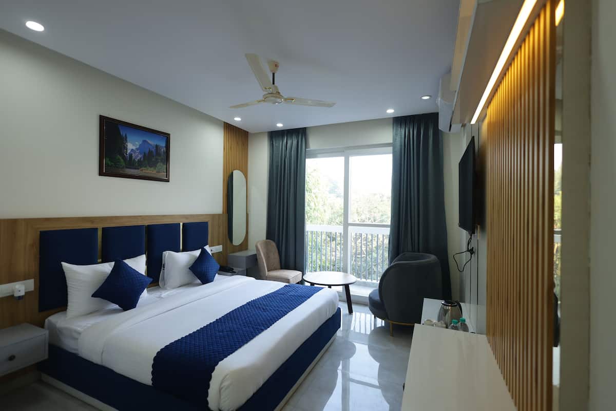 A hotel room with a large bed, a desk, a chair, a TV, and a balcony with curtains.
