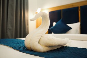 Een handdoek in de vorm van een zwaan op een bed met een blauwe deken, een houten hoofdbord en een donker gordijn op de achtergrond.