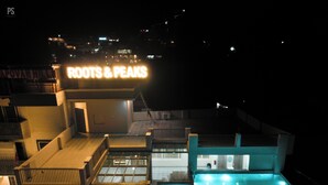 A modern hotel with a rooftop pool and a sign reading "ROOTS & PEAKS". - Roots & Peaks (Rishikesh)