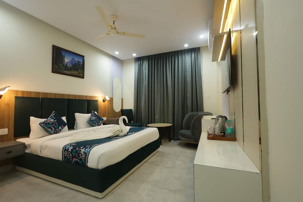 A hotel room with a bed, a desk, a chair, a ceiling fan, a painting, and a large window with curtains.
