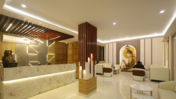 A modern reception area with a marble counter, wooden accents, and a Buddha statue in the background. - Roots & Peaks (Rishikesh)