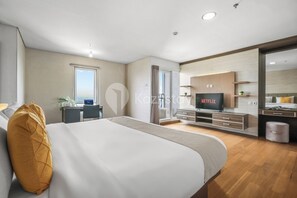 Ein modernes Hotelzimmer mit einem großen Bett, einem Schreibtisch mit Computer, einem an der Wand montierten Fernseher und einem Badezimmer mit Spiegel und Waschbecken.