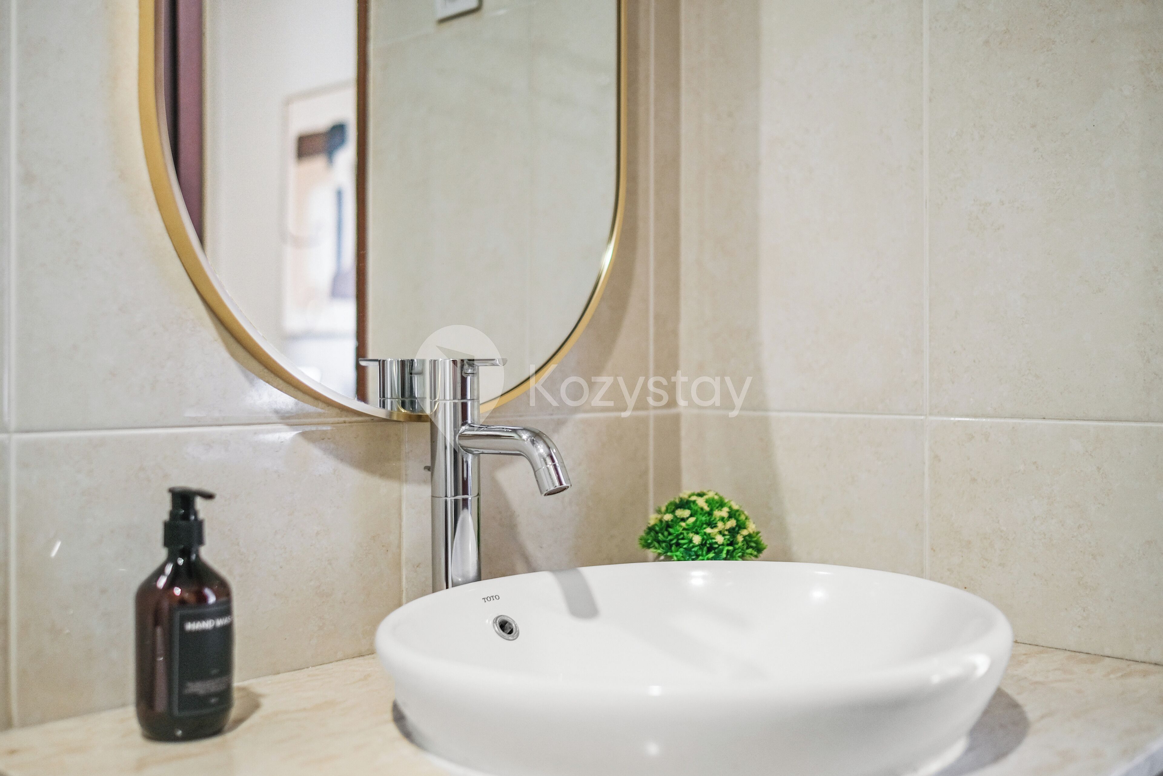 Baño con lavamanos blanco, espejo redondo, grifo cromado y una pequeña planta verde.
