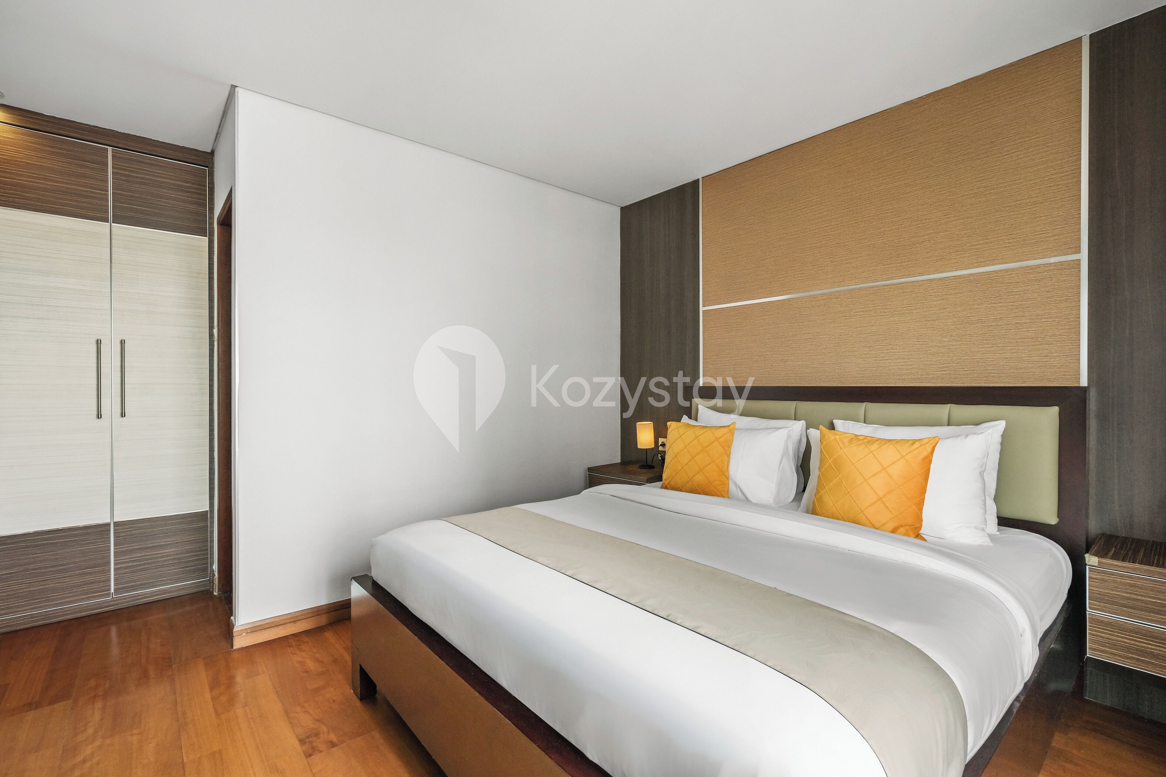 Ein modernes Hotelzimmer mit einem großen Bett, einem Kleiderschrank und einem Nachttisch mit einer Lampe.
