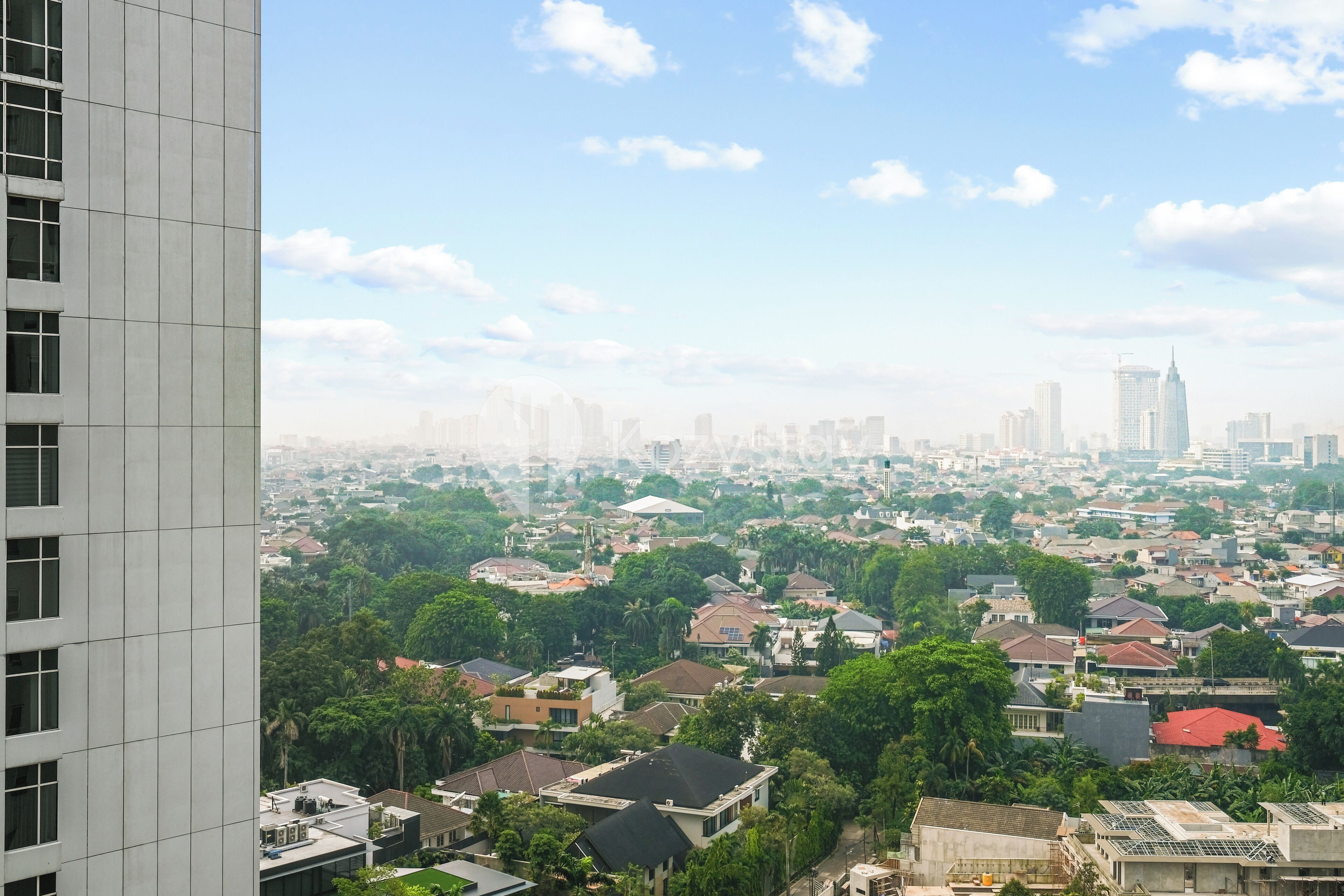 A high-rise building overlooking a densely populated urban area with numerous residential buildings and greenery.