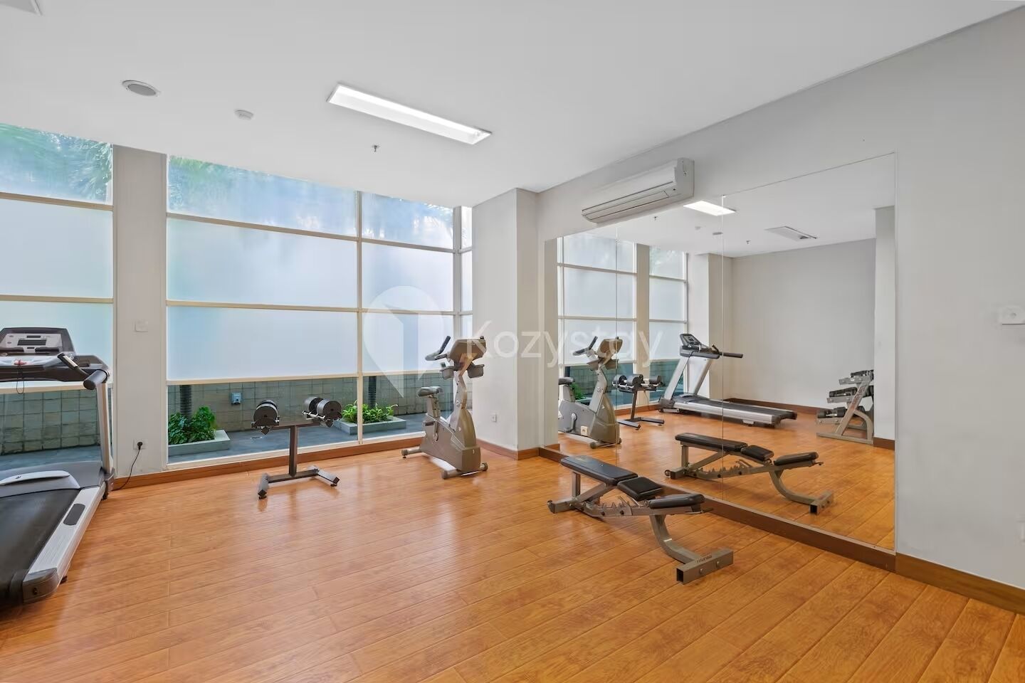 A gym with exercise equipment, large windows, and a wooden floor.