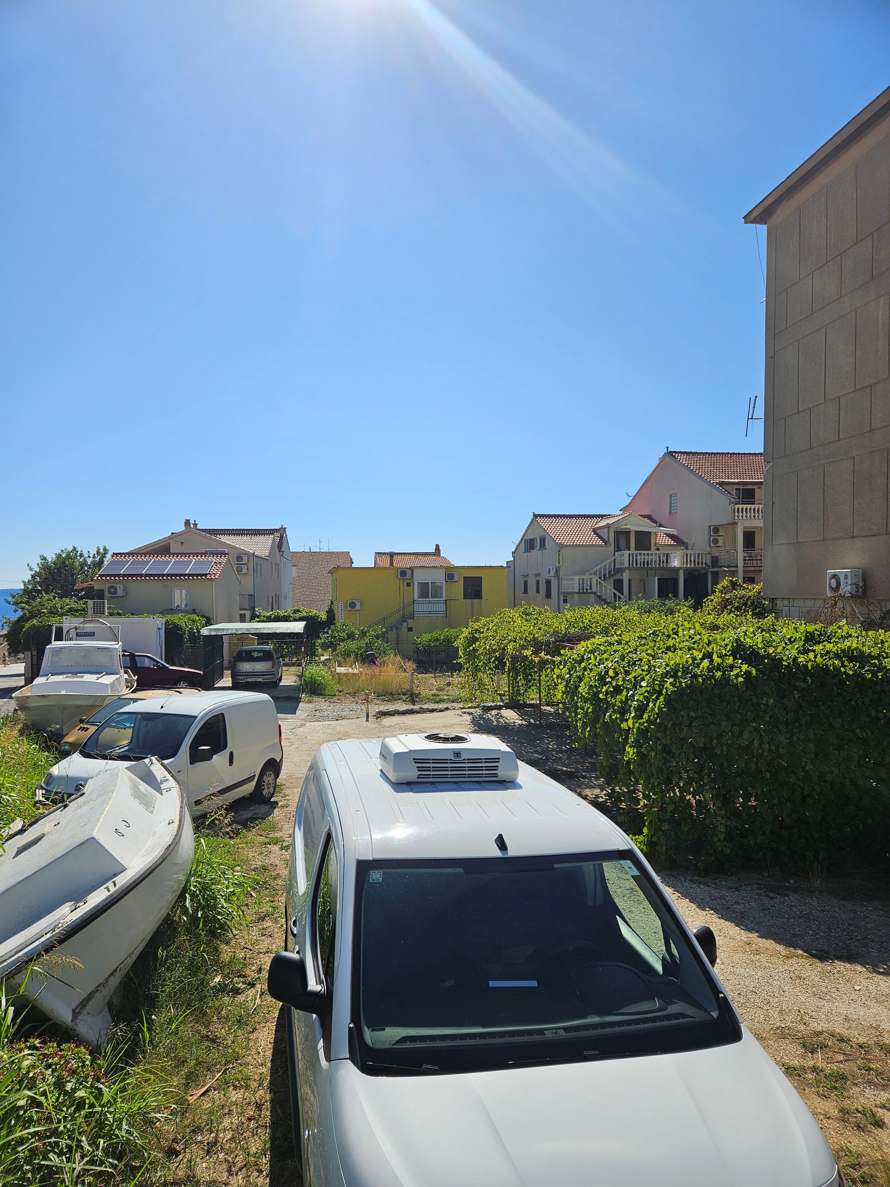 Uma carrinha branca estacionada num parque de estacionamento, com barcos e um edifício ao fundo.