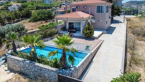A villa with a swimming pool, stone walls, and a patio area with palm trees. - Villa Irina by Estia (Heraklion)