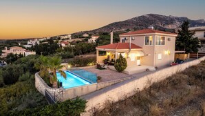 A modern villa with a swimming pool, a patio, and a view of a mountainous landscape. - Villa Irina by Estia (Heraklion)