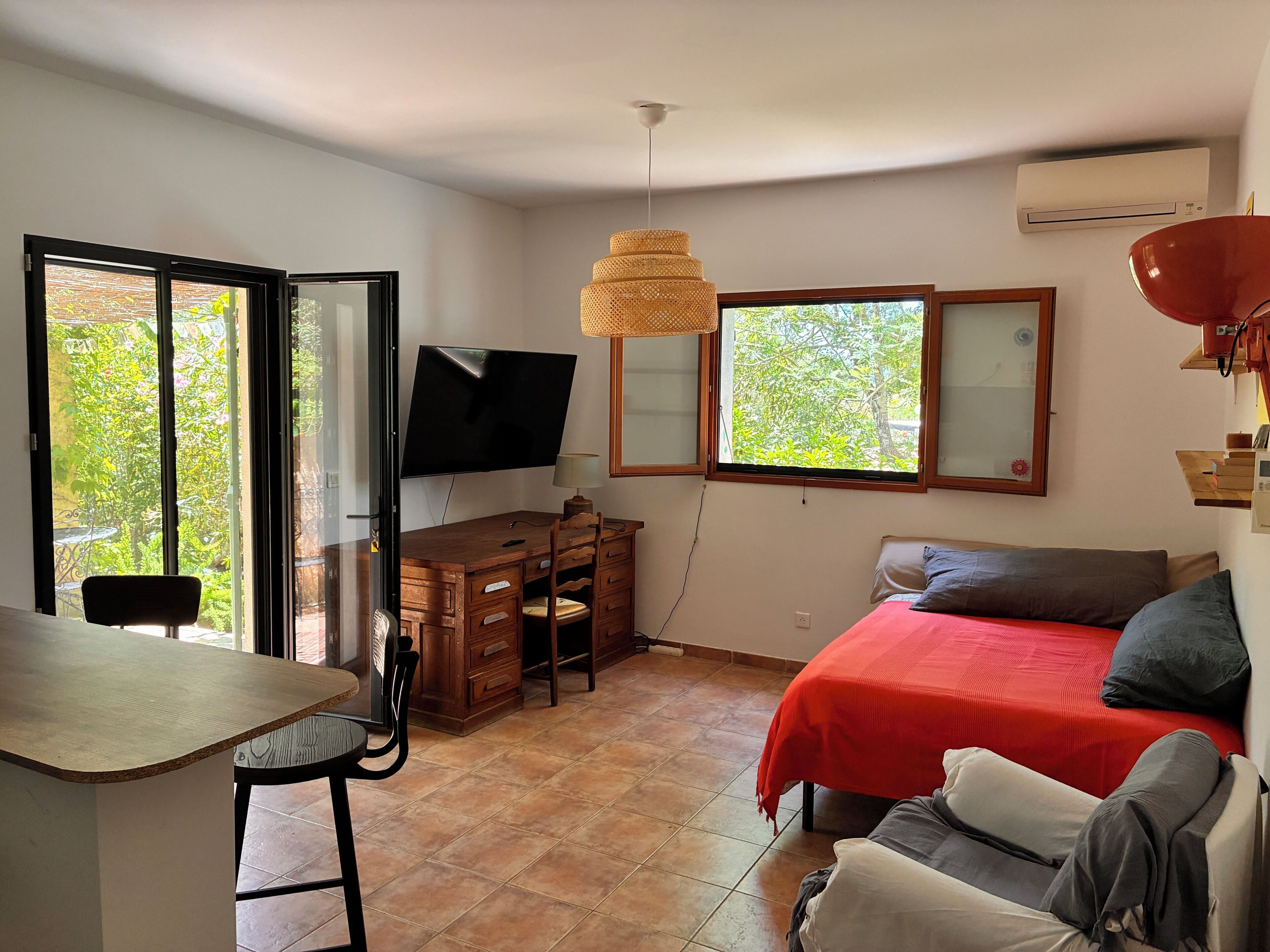 A room with a desk, chair, bed, and a TV mounted on the wall.