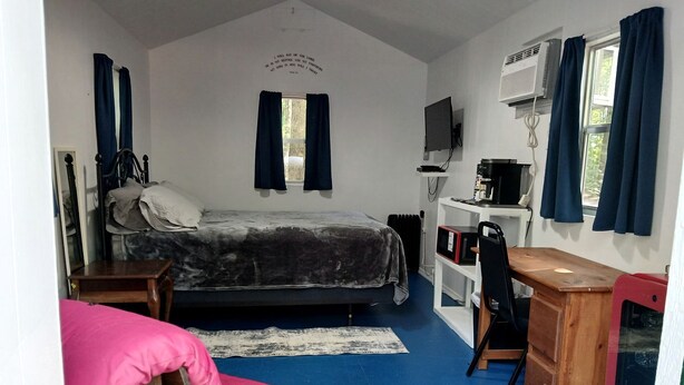 Une chambre à coucher avec un lit, un bureau, une chaise, un téléviseur et une fenêtre avec des rideaux.