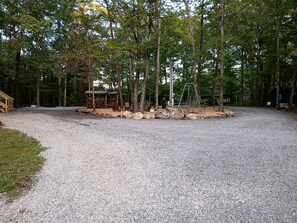 A gravel parking area with a swing set and a covered structure in a wooded setting. - Peaceful Bunkhouse Surrounded by Nature near Graysville, Tennessee (Graysville)