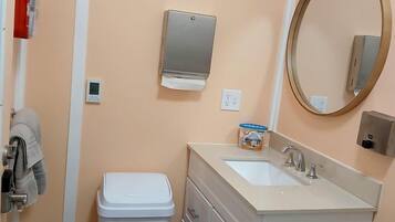 Une salle de bain équipée de toilettes, d’un lavabo, d’un miroir et d’une poubelle.