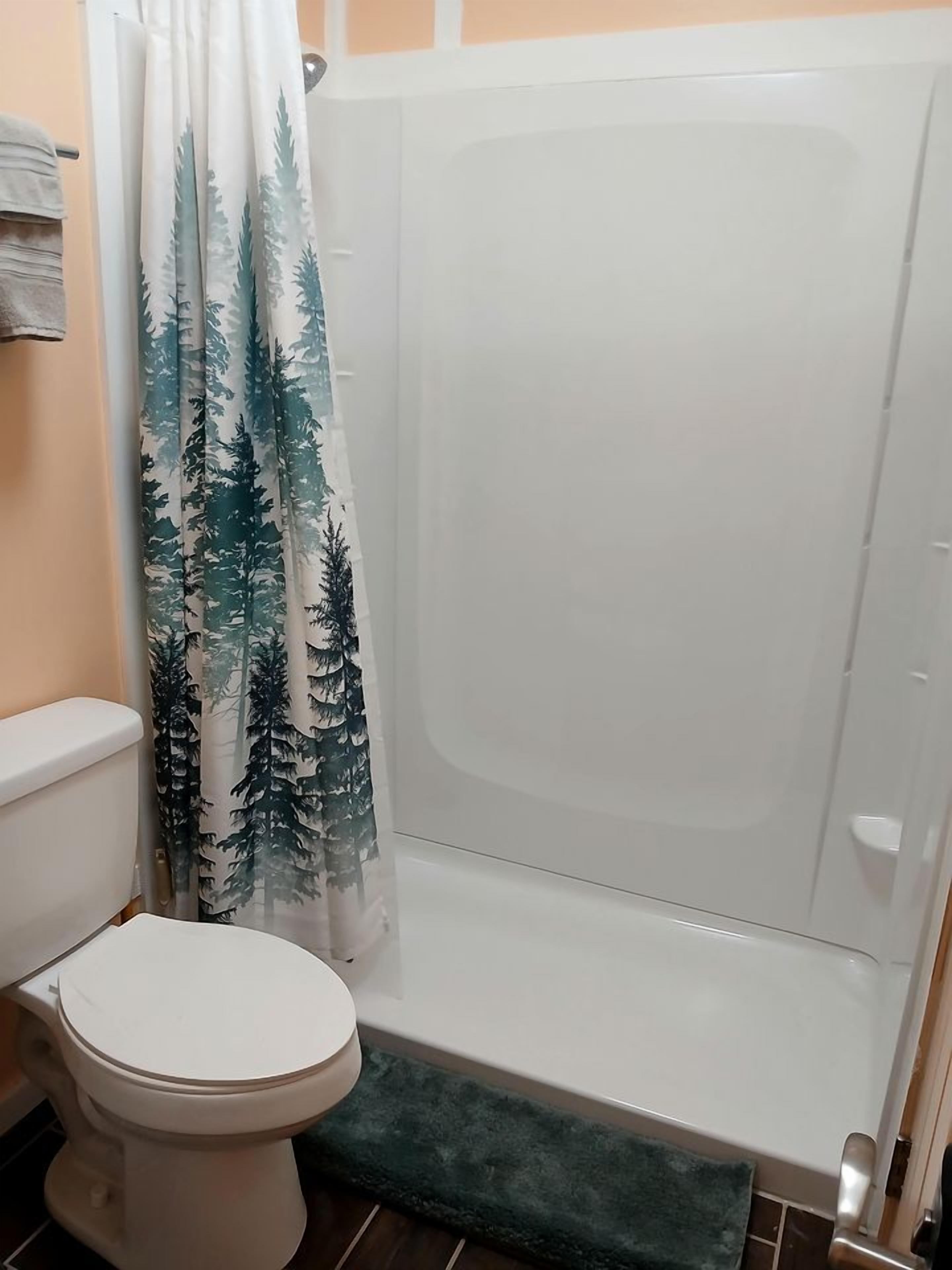 A bathroom with a shower, toilet, and a green bath mat.