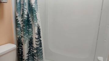 A bathroom with a shower, toilet, and a green bath mat.