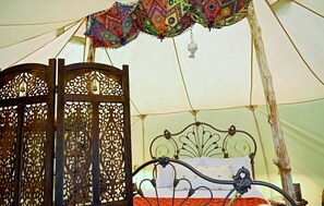 Une tente équipée d’un lit, de rideaux décoratifs et d  ’une cloche suspendue.