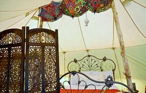 Una tienda de campaña con cama, cortinas decorativas y una campana colgante.