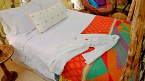 Ein ordentlich bezogenes Bett mit weißer Daunendecke und Kissen, einer farbenfrohen Steude und einem weißen Bademantel.