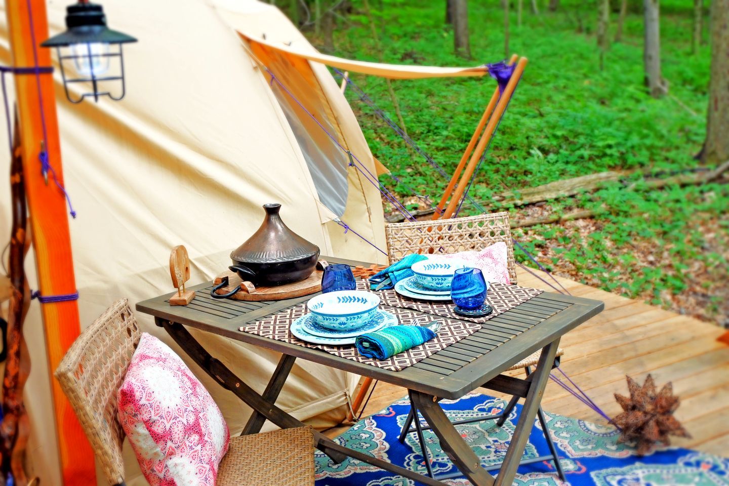 A camping setup with a tent, a table with plates, a pot, and a lantern.