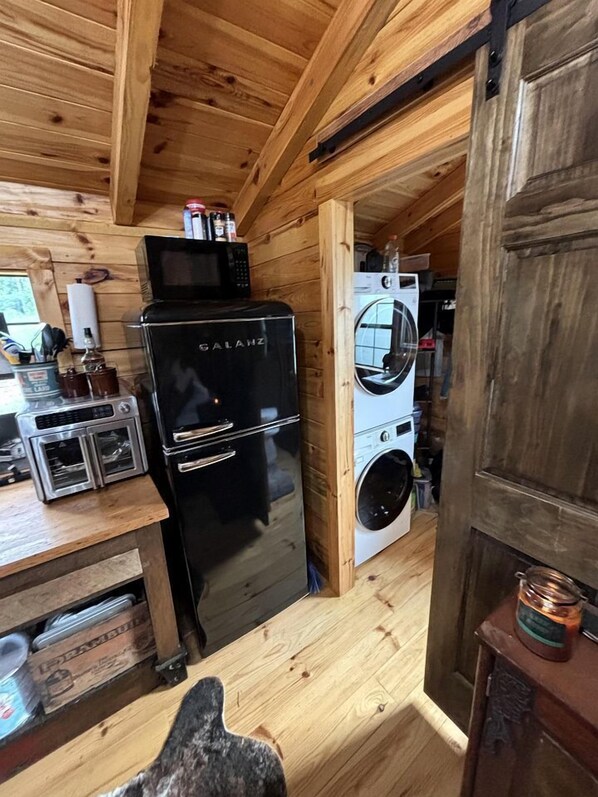 Eine kleine Küche mit einem schwarzen Galanz-Kühlschrank, einer Mikrowelle, einer Waschmaschine und einem kleinen Schrank mit Küchenutensilien.