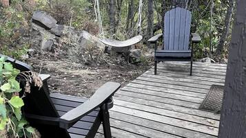 Une terrasse en bois avec deux fauteuils Adirondack, entourée d’une zone boisée.