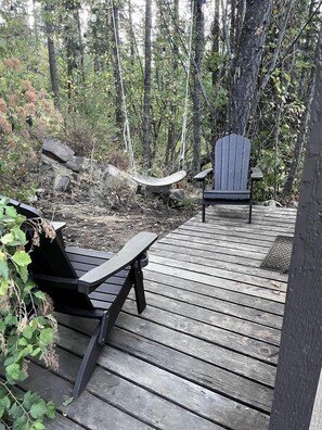 Een houten terras met twee Adirondack stoelen, omringd door bebossing.