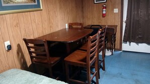 A wooden-paneled room with a dining table, chairs, a television, and a fire extinguisher.