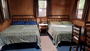 Ein Zimmer mit zwei Betten, einem kleinen Tisch mit Büchern, einem Stuhl und einem Fenster.