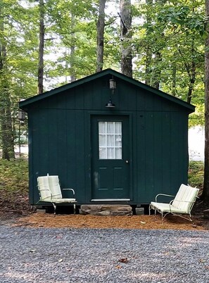 A small green wooden cabin with a door and two white chairs outside. - Cozy Bunkhouse for Two Nestled in the Trees near Graysville, Tennessee (Graysville)