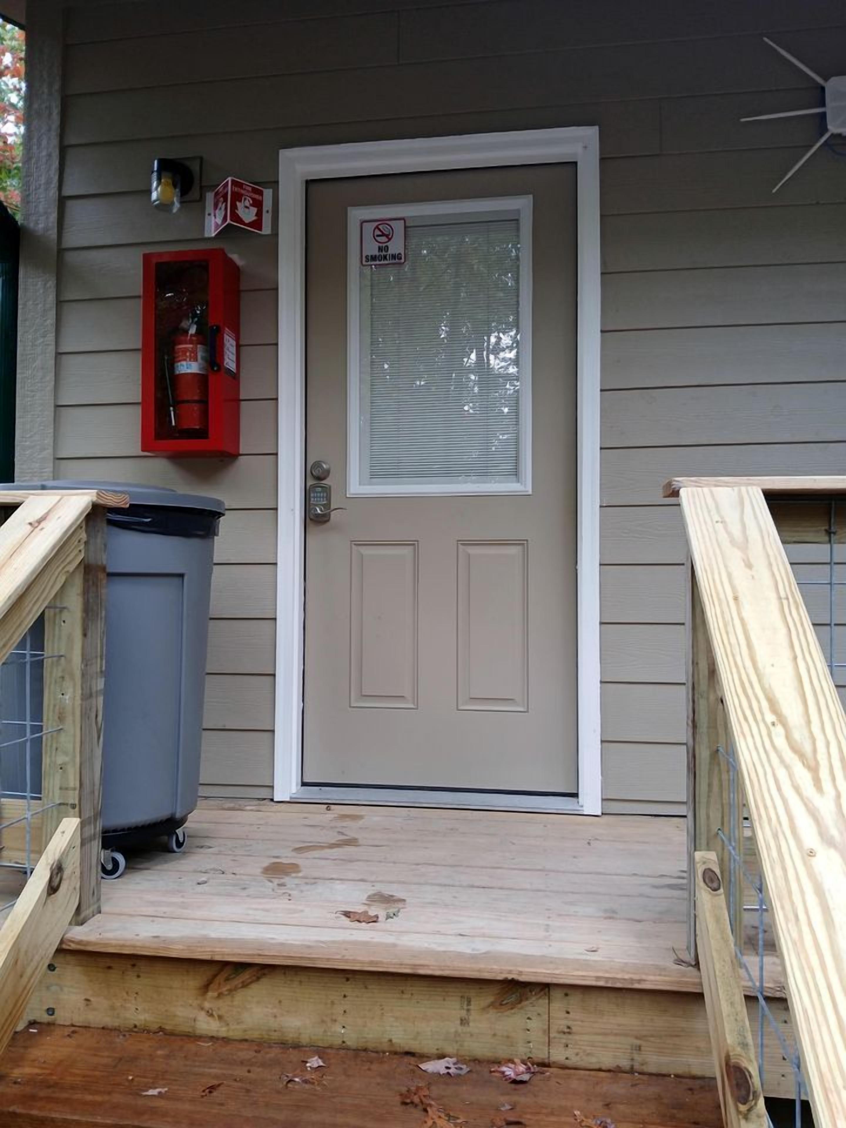 A front door with a 'No Smoking' sign, a fire extinguisher, and a trash can outside.
