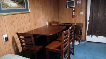 A wooden-paneled room with a dining table, chairs, a television, and a fire extinguisher.