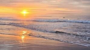 Una playa al atardecer con olas y una persona en el agua.