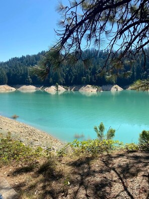 Paisagem natural com um lago límpido, rodeado por floresta densa e terreno rochoso.