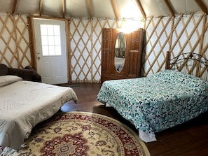 A cozy bedroom with two beds, a wooden wardrobe, a mirror, and a patterned rug.
