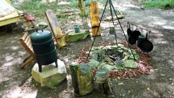 Ein rustikaler Außenbereich zum Kochen mit Grill, Töpfen und einem Wasserspeicher.