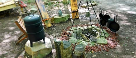 A rustic outdoor cooking area with a grill, pots, and a water container.
