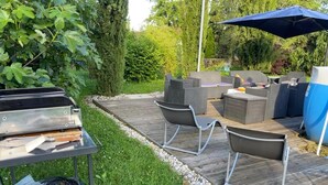 An outdoor patio with a grill, two chairs, a table, and a blue umbrella. - La Tramolière, accommodation in a green setting (Le Passage)