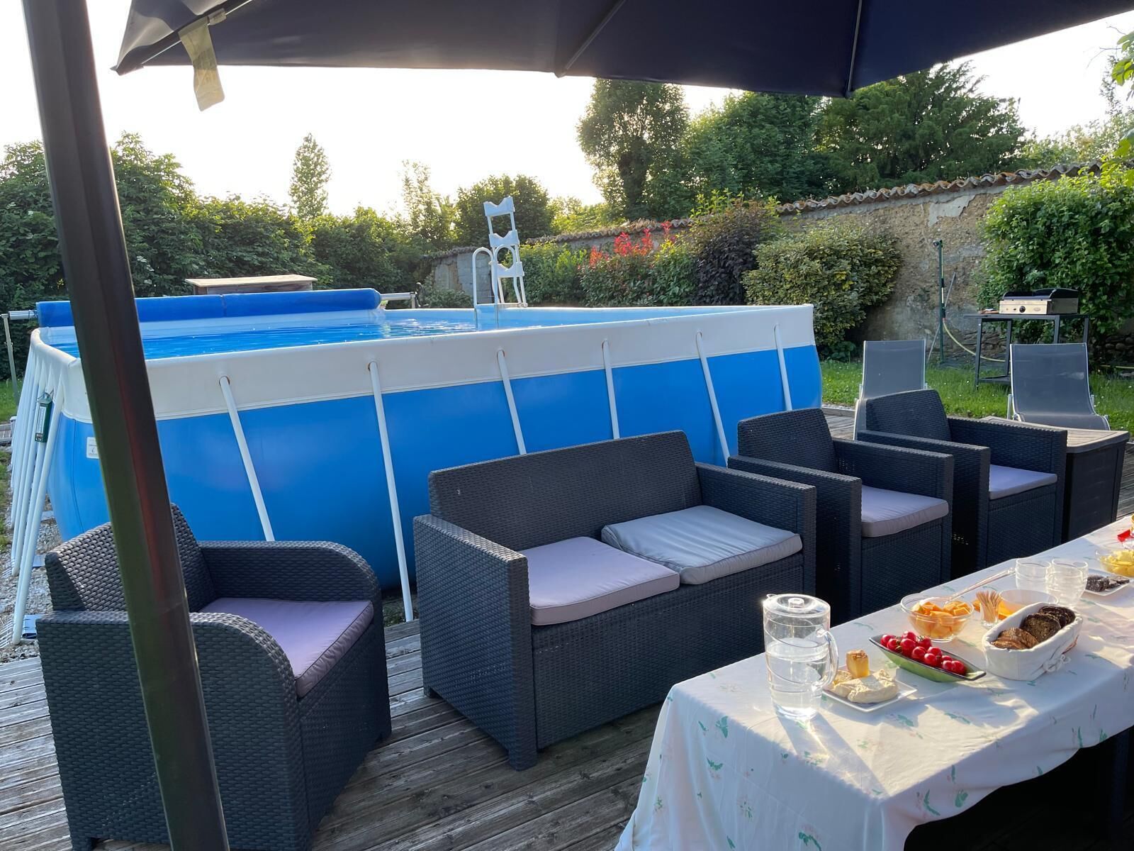 Uma área de piscina ao ar livre com um terraço coberto, móveis de vime e uma mesa posta para refeição.