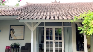 A building with a tiled roof, a covered entrance with glass doors, and a framed picture on the wall. - Tropical Oasis 2 BR Villa Near Beach (Seminyak)