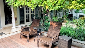 An outdoor seating area with wicker furniture and a glass table, surrounded by lush greenery and a covered patio. - Tropical Oasis 2 BR Villa Near Beach (Seminyak)